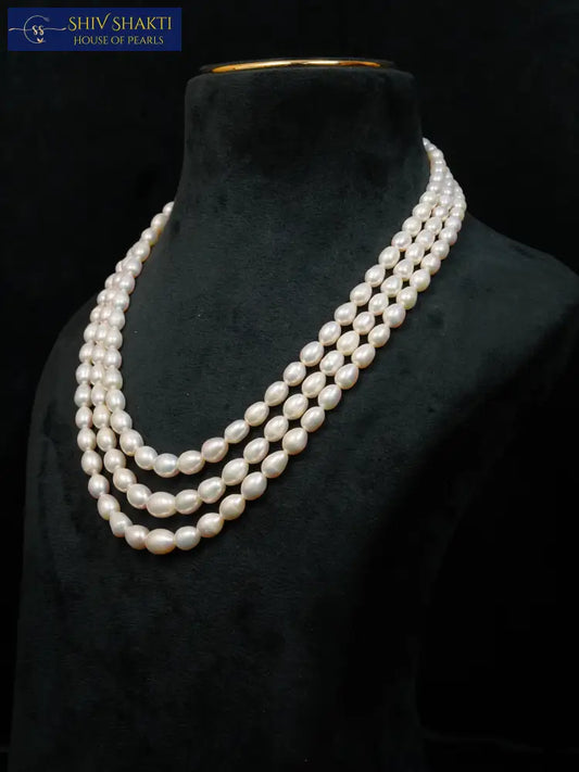 Three-strand pearl necklace on a black mannequin against a black background