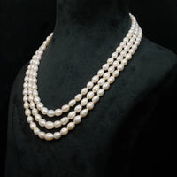 Three-strand pearl necklace on a black mannequin against a black background